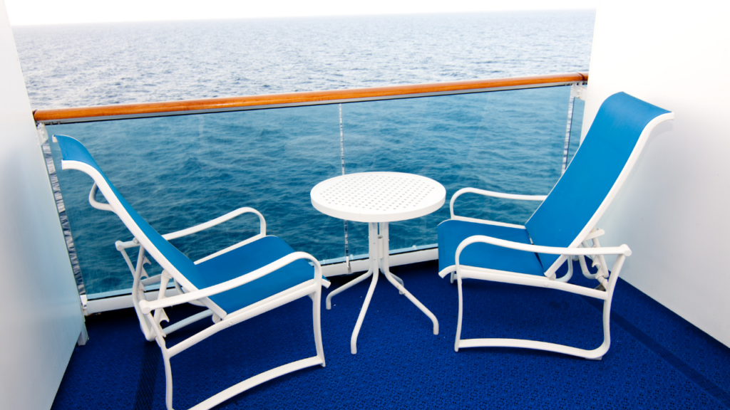 クルーズ客船のベランダ、白と青色の椅子が２つと、その間に白いテー物が一つ。お部屋から眺めている様子で、背景は海。